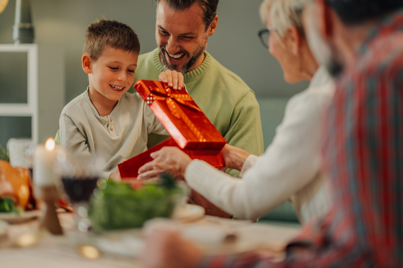 father and son opening a present with grandparents at Christmas